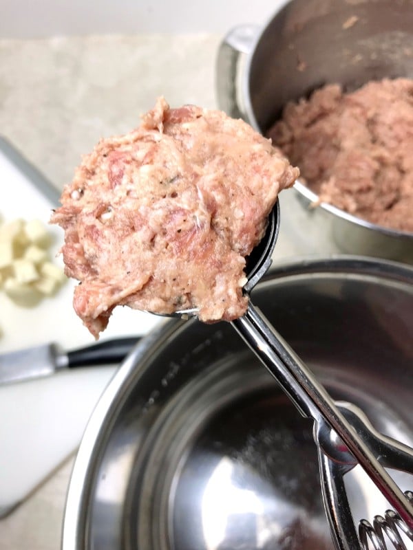 a cookie scoop full of meat above 2 pans, one is full of the meat mixture