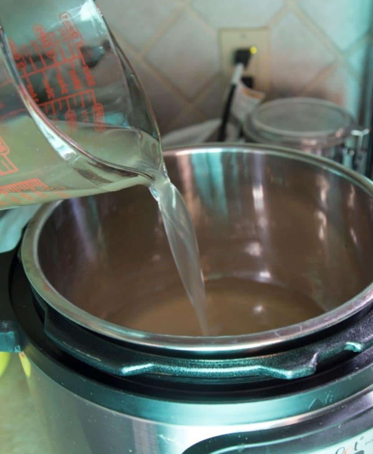 Broth being poured from a glass measuring cup into an instant pot.