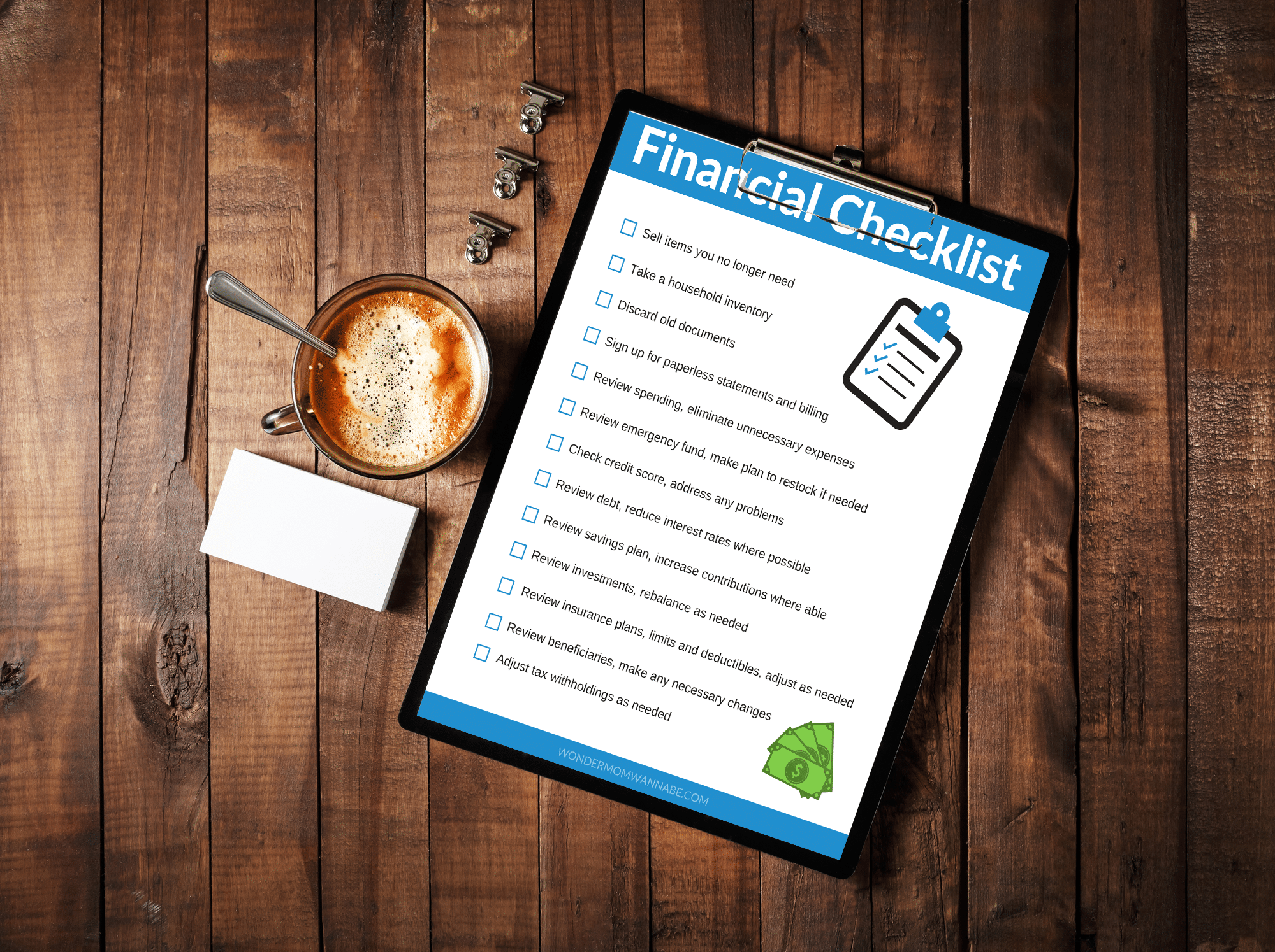a printable financial checklist on a clipboard next to clips, a cup of coffee and white sticky notes, all on a table