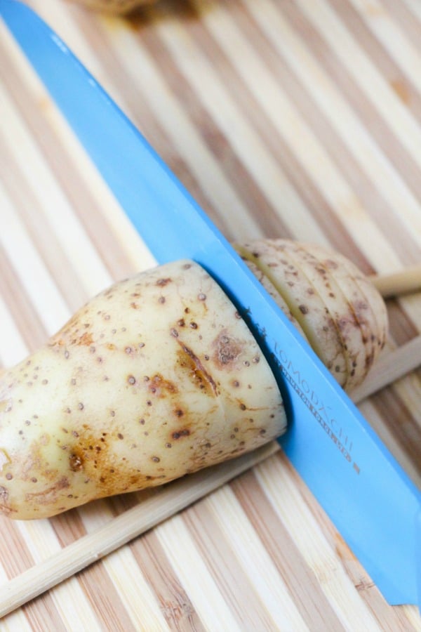 a potato on a table in between chopsticks with a knife slicing into it