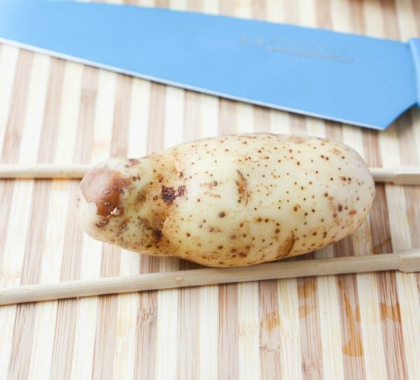 a potato on a table in between chopsticks and next to a knife