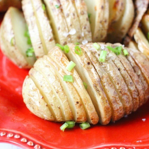 sliced baked potatoes on a red plate topped with green onions