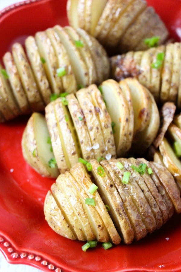 sliced baked potatoes on a red plate topped with green onions