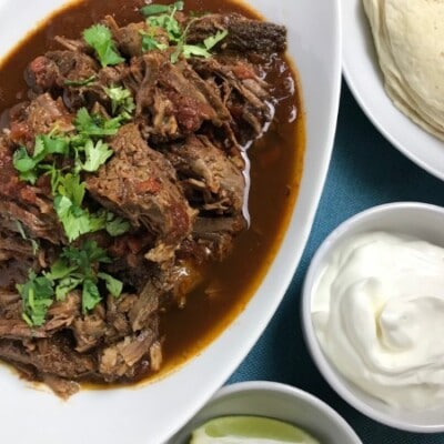 Instant Pot Carne Guisada in white serving dish with side dishes of sour cream and tortillas