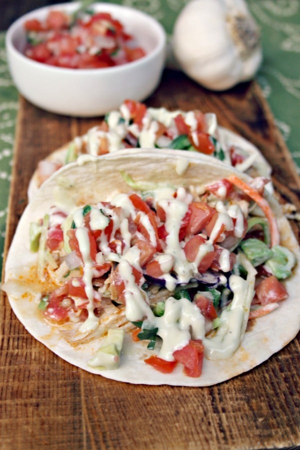 chicken enchiladas, a white bowl of salsa and garlic on a wooden cutting board