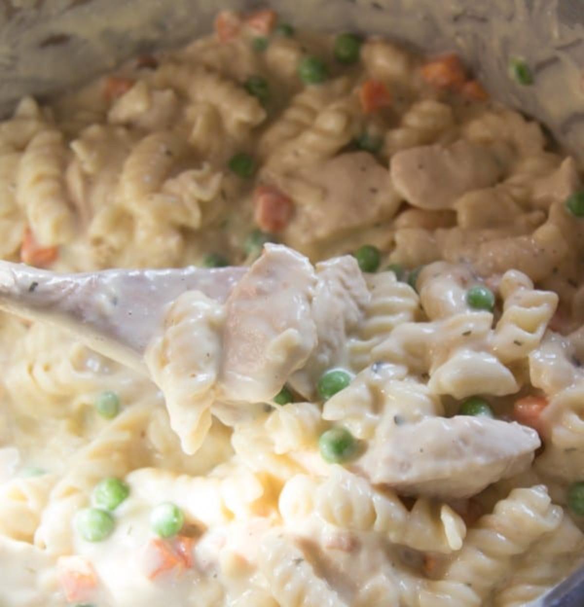 A spoon holding some creamy chicken pasta above an instant pot filled with the pasta.