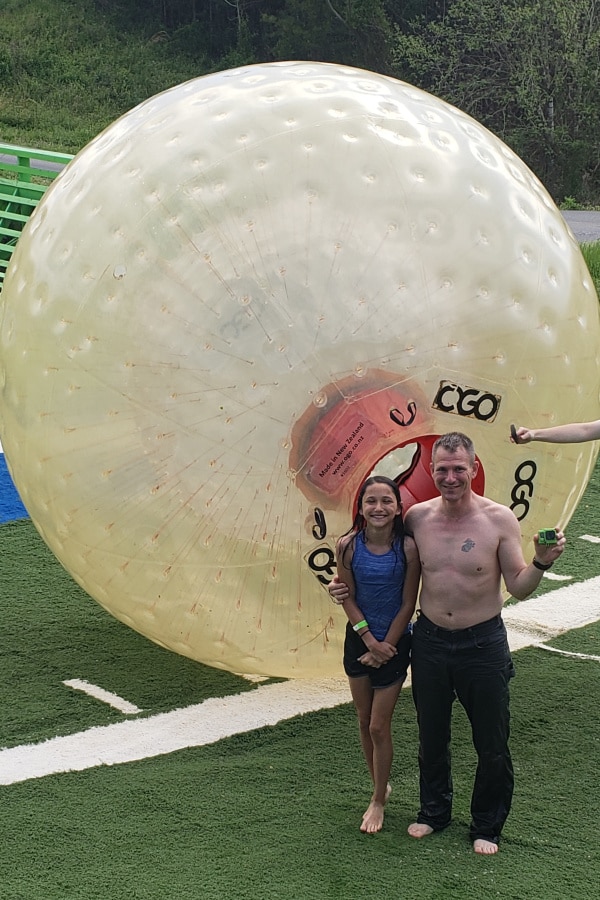 a father and daughter outside next to a giant ball people can ride in