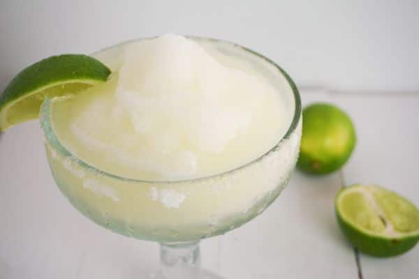 Classic frozen margarita on table with lime wedge on rim and limes in background