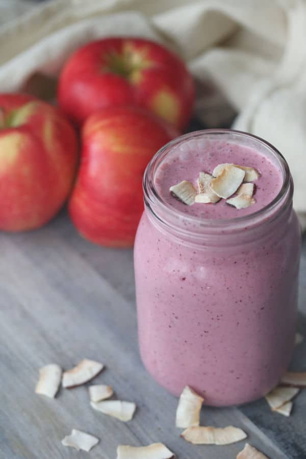 cranberry apple smoothie in a glass jar with apples in the background