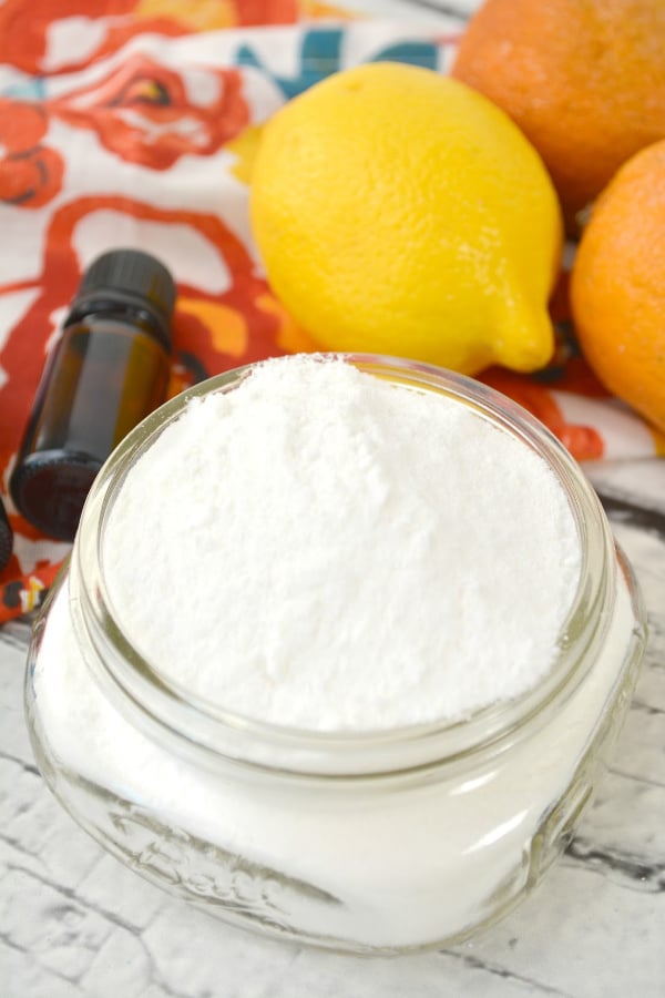 DIY dishwasher detergent in a glass jar with a glass container and a lemon and oranges in the background