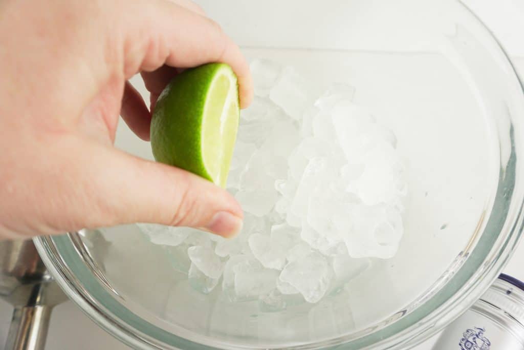 squeezing limes over a glass bowl of ice for a restaurant-style classic frozen margarita