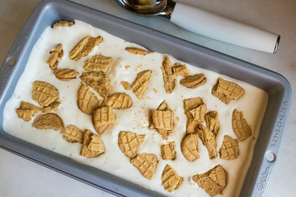 ice cream topped with crumbled nutter butter cookies in a baking dish with an ice cream scoop next to it