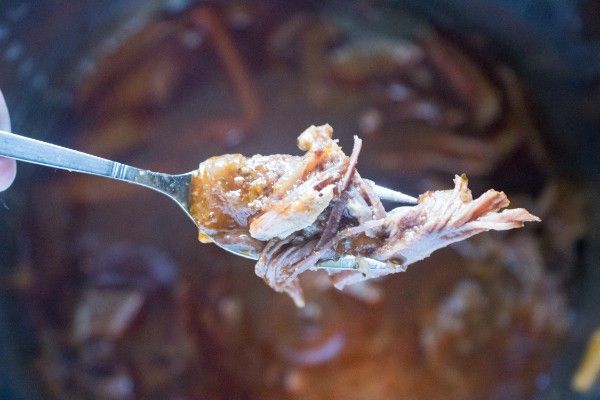 a fork holding shredded beef above an instant pot filled with the beef