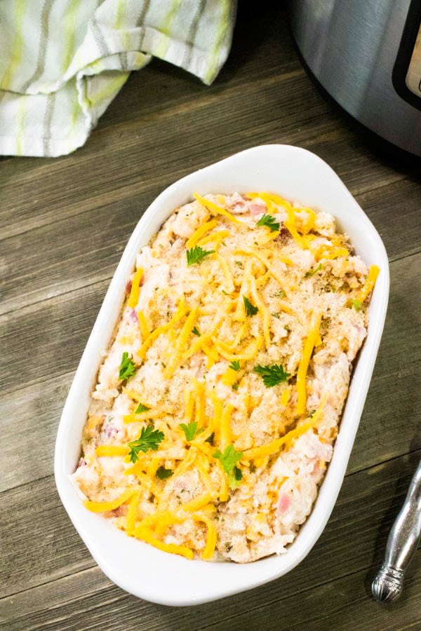 Cheesy Potato Casserole in a white baking dish on table next to Instant Pot and serving spoon
