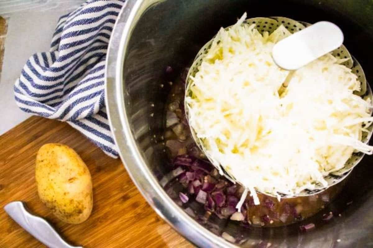a steamer basket full of shredded potatoes in an instant pot with onions, and broth under it.