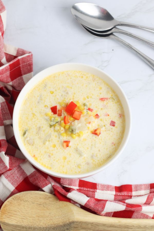 bowl of corn chowder with corn kernels and chopped red bell pepper garnish and spoons in background