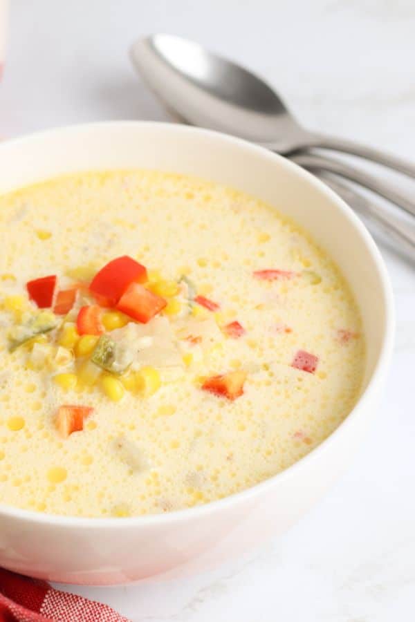 bowl of corn chowder with corn kernels and chopped red bell pepper garnish and spoons in background