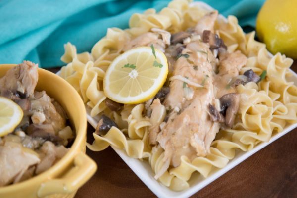 a bowl and a plate of noddles topped with lemon chicken, mushrooms, and a lemon slice