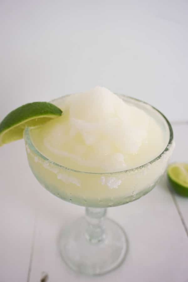 classic frozen margarita with lime wedge and salt on rim, half lime on table in background