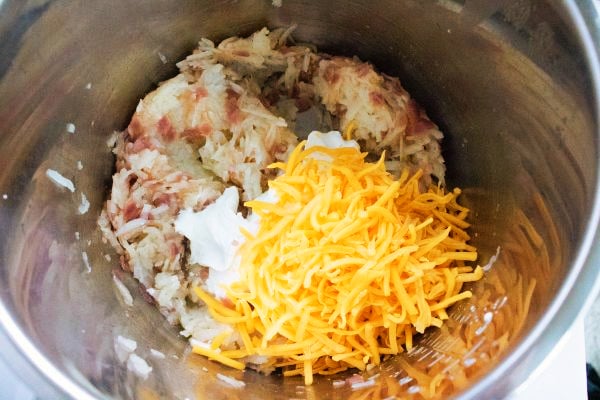 cooked shredded potatoes topped with sour cream and shredded cheese in an instant pot