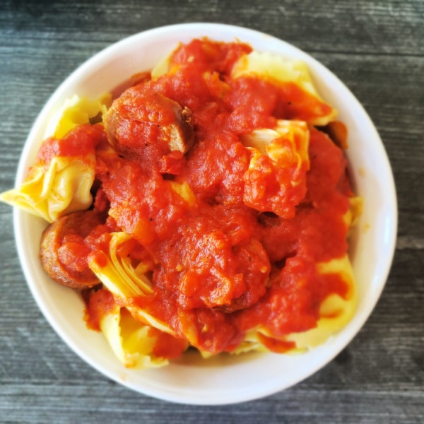 white bowl filled with tortellini and sausage and topped with pasta sauce
