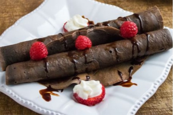 Chocolate Crepes on a white plate topped with raspberries 