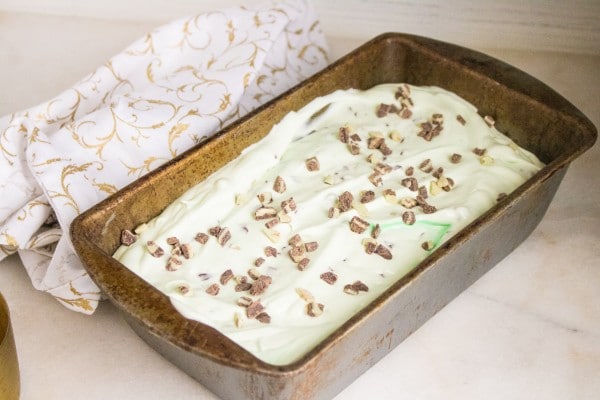 freezer container pan of homemade mint chip ice cream next to a white and gold cloth on a white table