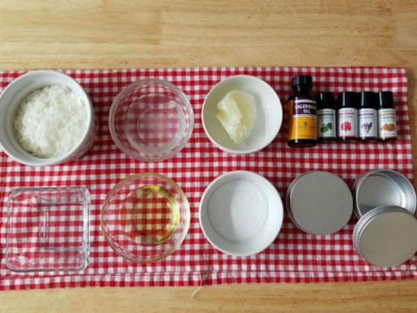 ingredients for essential oil itch relief cream in white bowls and glass bowls on a checkered linen