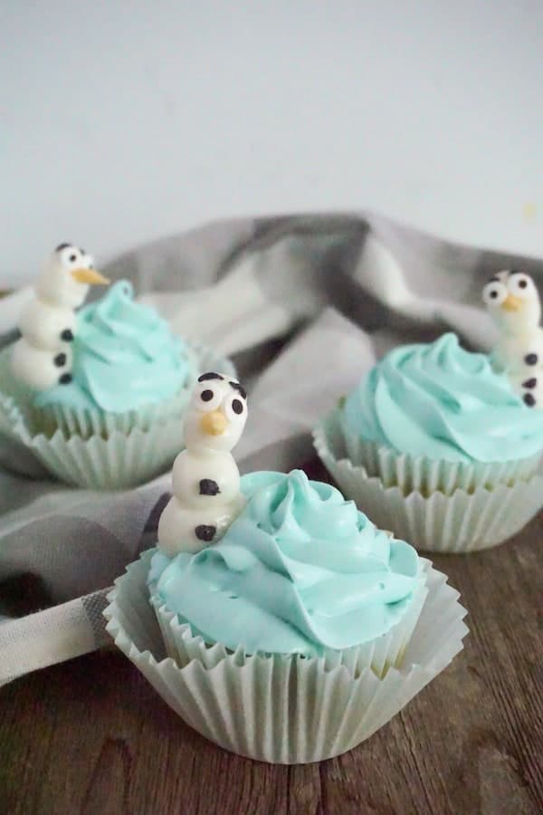 three Olaf cupcakes on a wood table with a grey and white linen in the background
