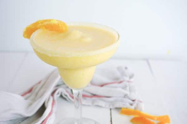 an orange creamsicle margarita in a glass on a white table 