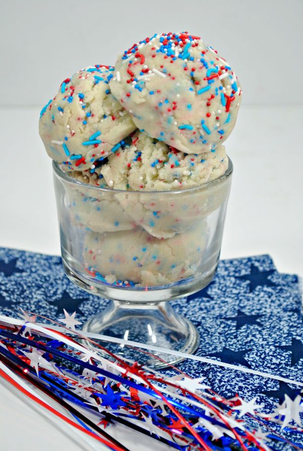 a glass bowl filled with Patriotic Edible Cookie Dough on a blue linen with star ribbons next to it