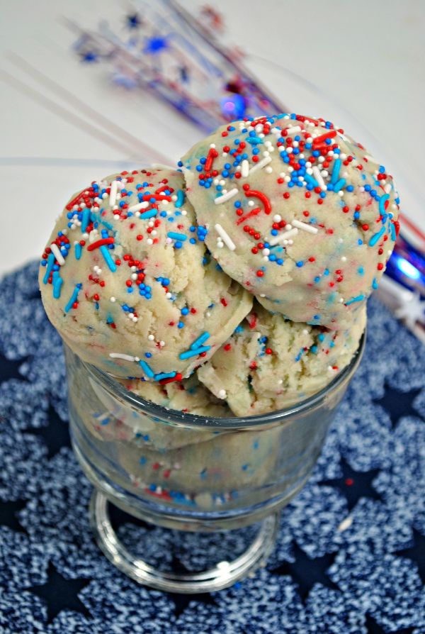 a glass bowl filled with Patriotic Edible Cookie Dough on a blue linen with star ribbons next to it