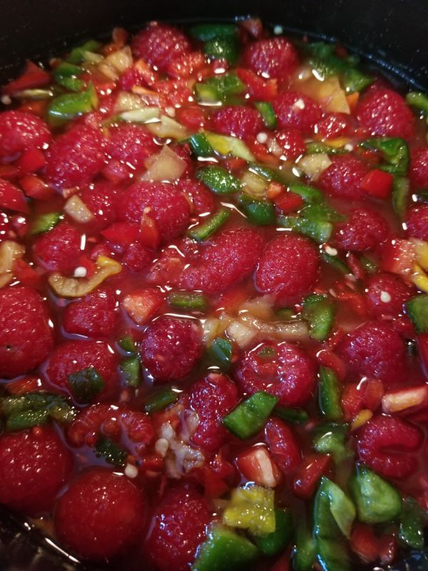 a saucepan filled with sugar, raspberries, vinegar and peppers