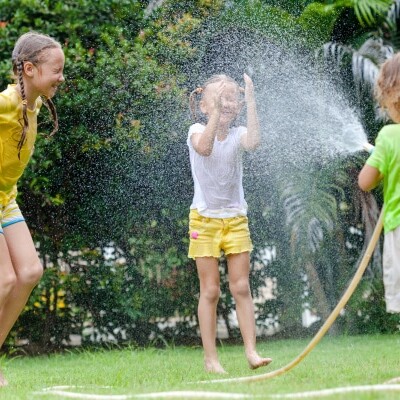 little boy is pouring a water from a hose at his sisters