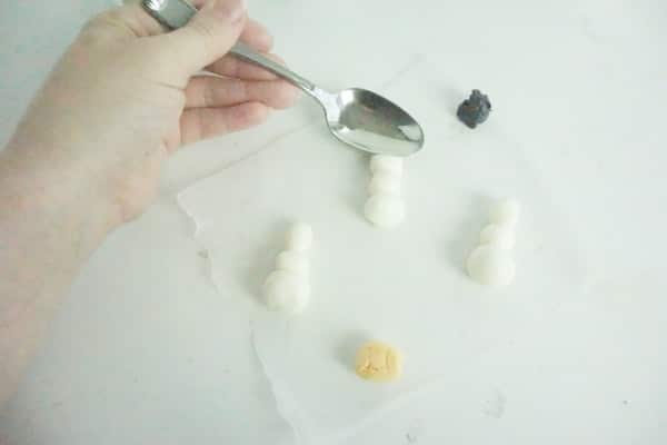 spoon being pressed into the top half of the marshmallow fondant snowman's face in order to create the olaf face structure on a white table