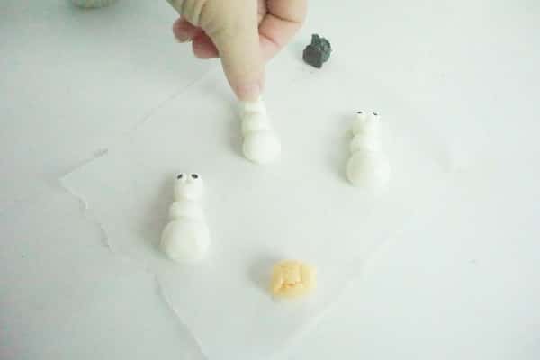 hand pressing fingernail into marshmallow fondant to form smile in olaf characters on a white table