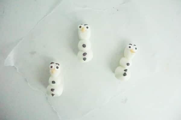 three olaf characters made from marshmallow fondant half-formed laying on a white table