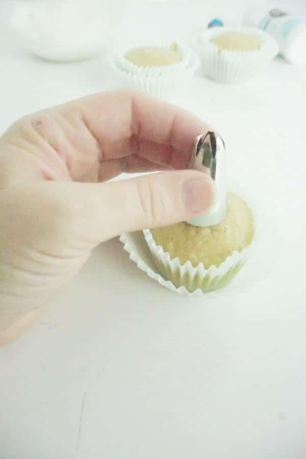 hand pressing a decorating tip into a cupcake top to create a well on a white table
