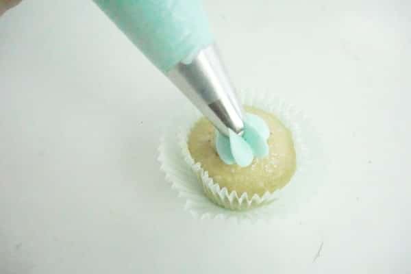 blue icing being placed on a cupcake with a decorating tip on a white table