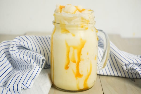 caramel flavored ice drink in a mason jar mug on a grey wood table with a white and blue linen