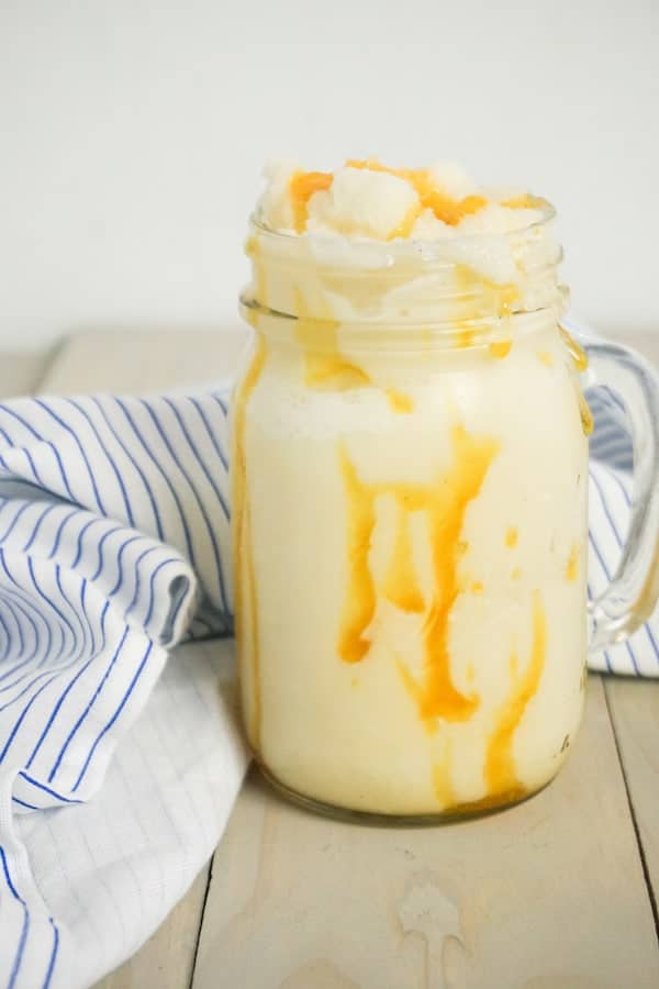 side view of a jar of caramel-flavored frappuccino on a grey wood background with a white and blue striped linen