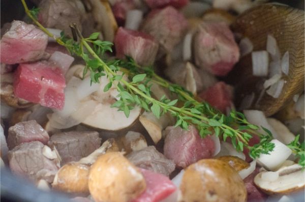 beef, mushrooms and onions in a pot topped with thyme