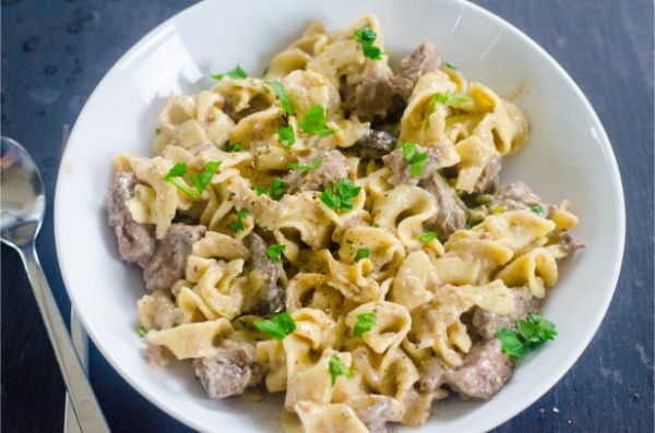 beef stroganoff in a white bowl on a black table next to a spoon