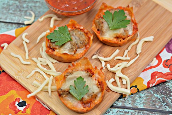mini meatball appetizer cups on a cutting board with shredded mozzarella cheese around them