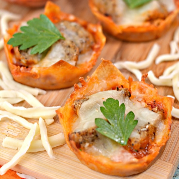 mini meatball appetizer cups on a cutting board surrounded by shredded mozzarella cheese