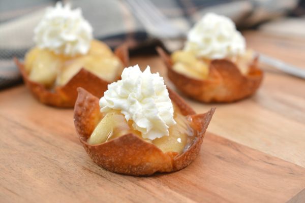 apple pie bites topped with whip cream on a wooden cutting board