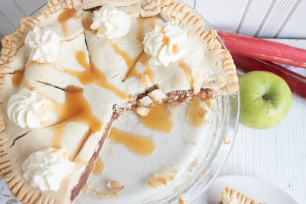 Apple and Rhubarb Pie topped with caramel and whip cream next to an apple