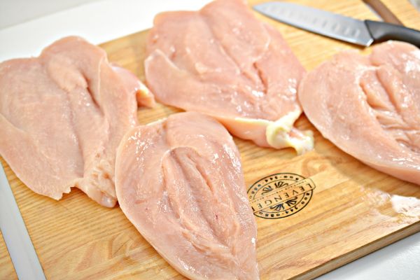 raw chicken breasts slit down the center next to a knife on a wood cutting board