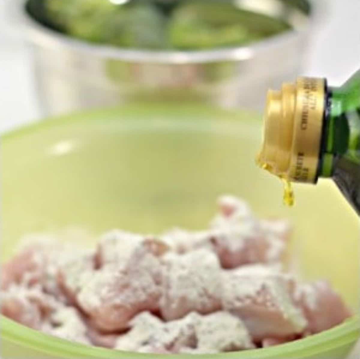 In a mixing bowl, the olive oil is being poured onto the chicken.