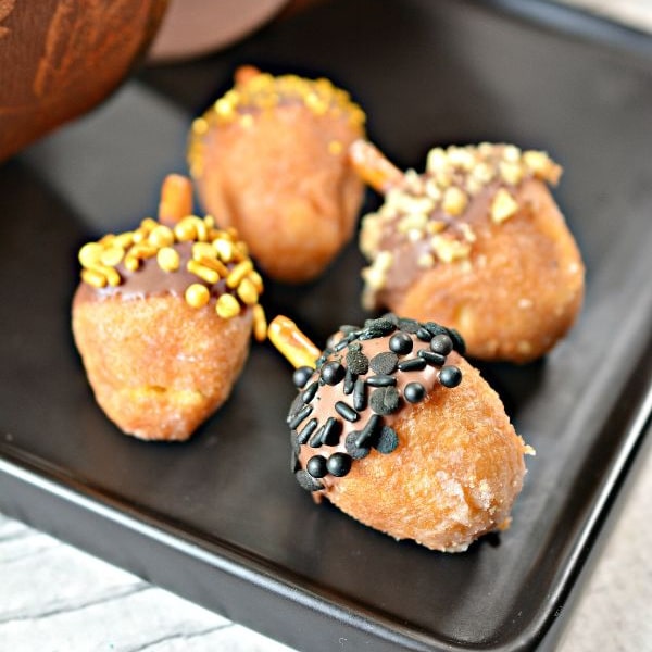 donut holes in the shape of acorns topped with sprinkles and a pretzel on a baking sheet